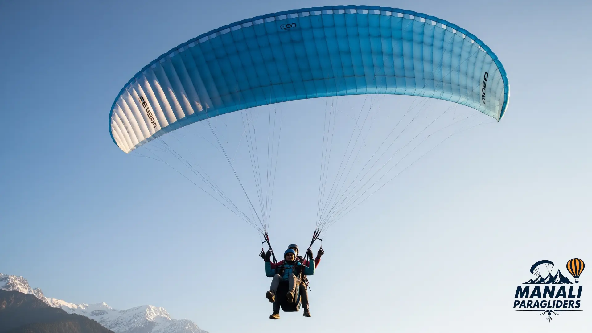 Tandem paragliding flight with Kullu Manali Paragliders over the Beas River and green valleys towards snowy Himalayan peaks.